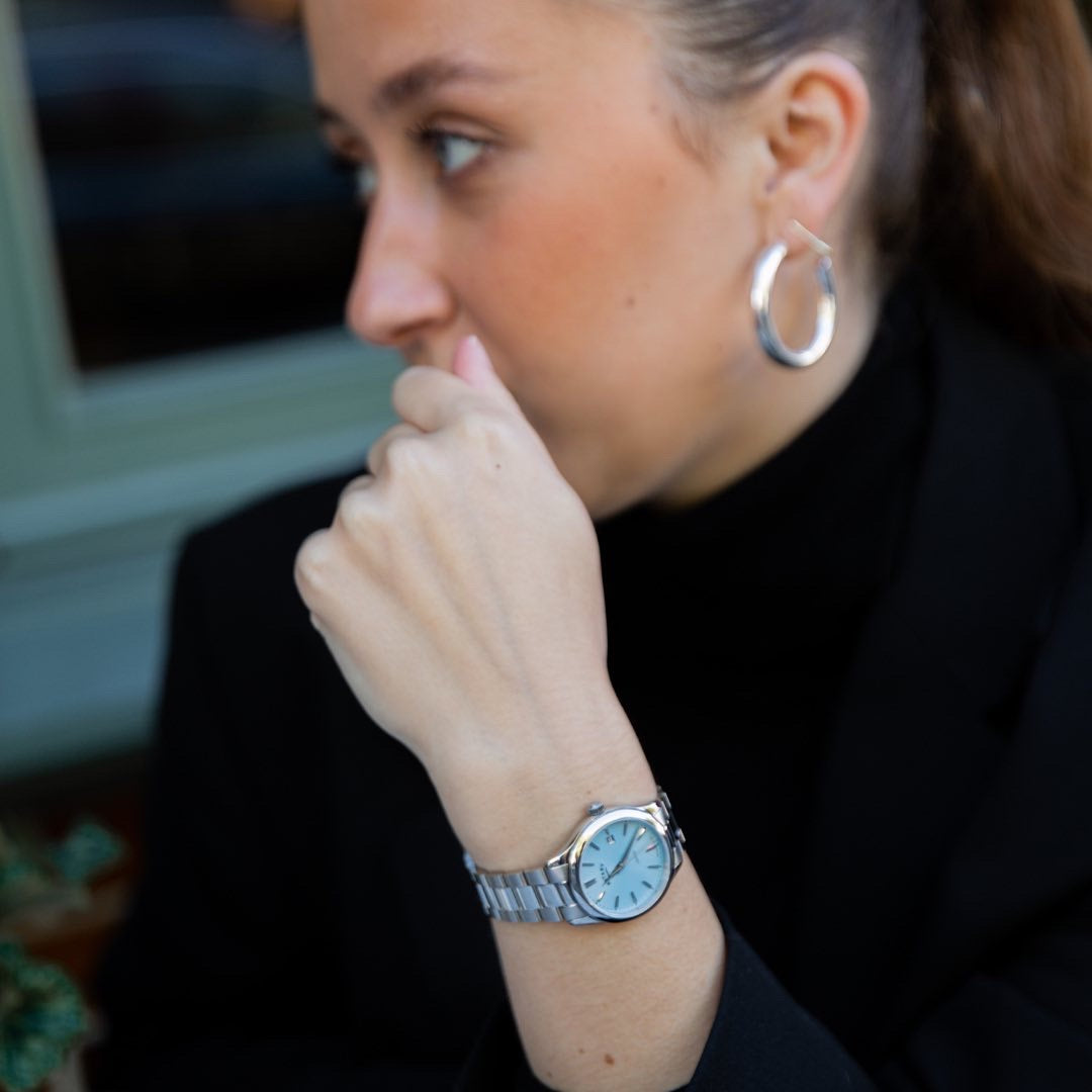 a woman wearing a rotary contemporary pastel watch with a blue in stainless steel. The woman is wearing black clothing and silver coloured jewellery