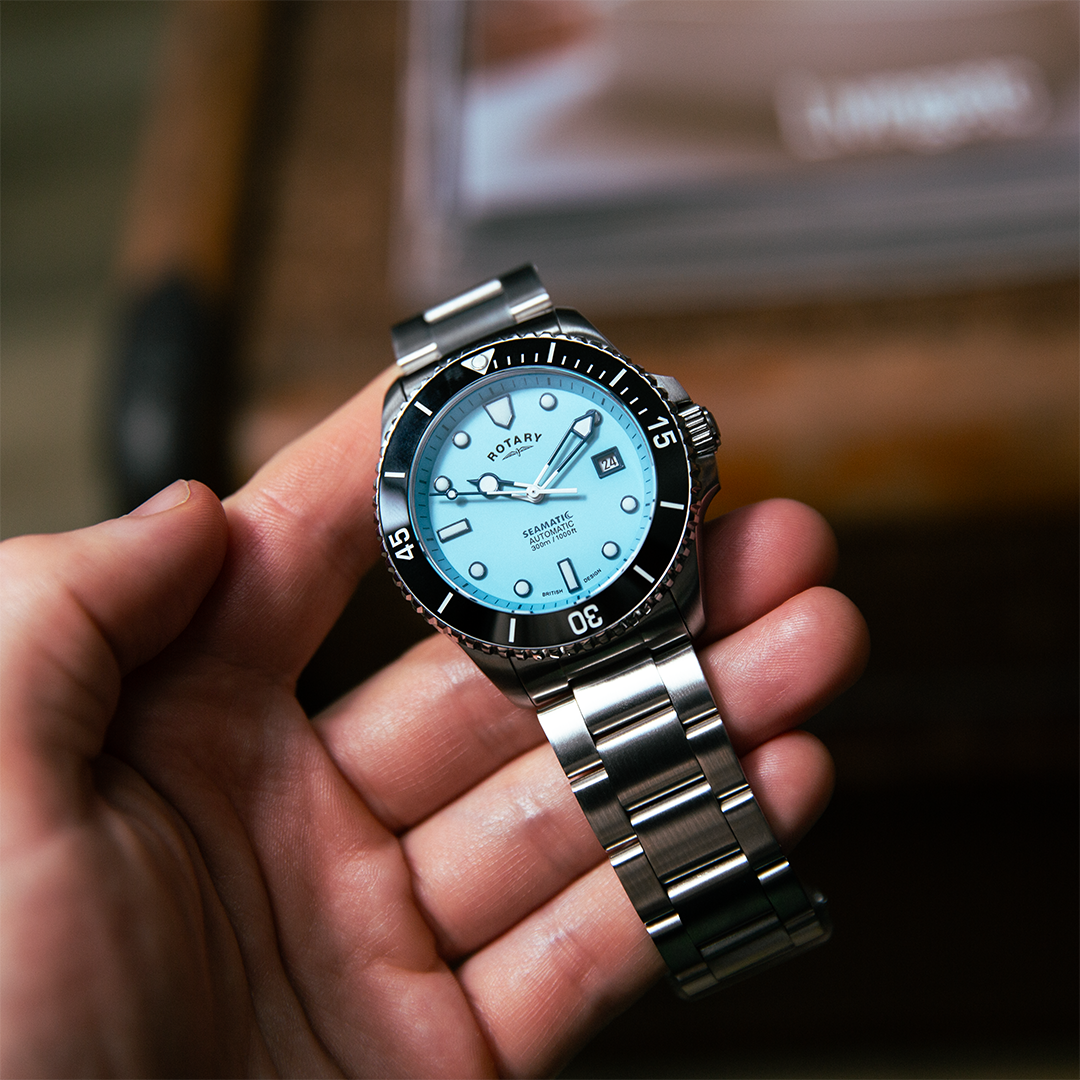 A Rotary Seamatic dive watch in stainless steel with a baby blue dial and a black ceramic bezel. The watch is pictured being held in a man's hand