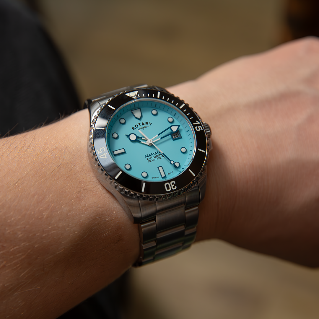 A Rotary Seamatic watch in stainless steel with a baby blue dial, black ceramic bezel and white hands. The watch is pictured on a wrist