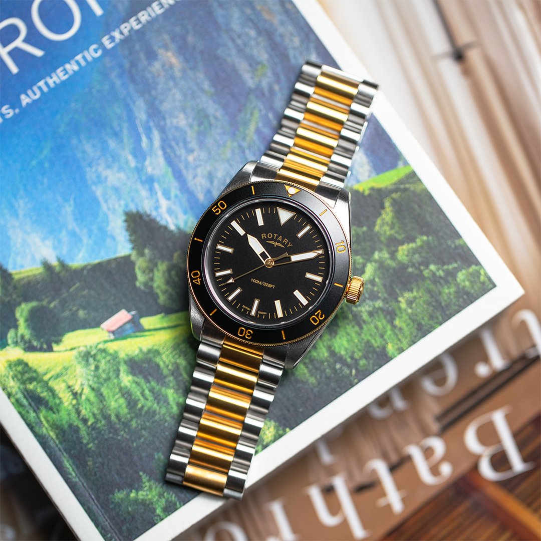 A Rotary heritage sport watch in two tone stainless steel and gold with a black dial and black bezel. The watch is pictured on a stack of books.