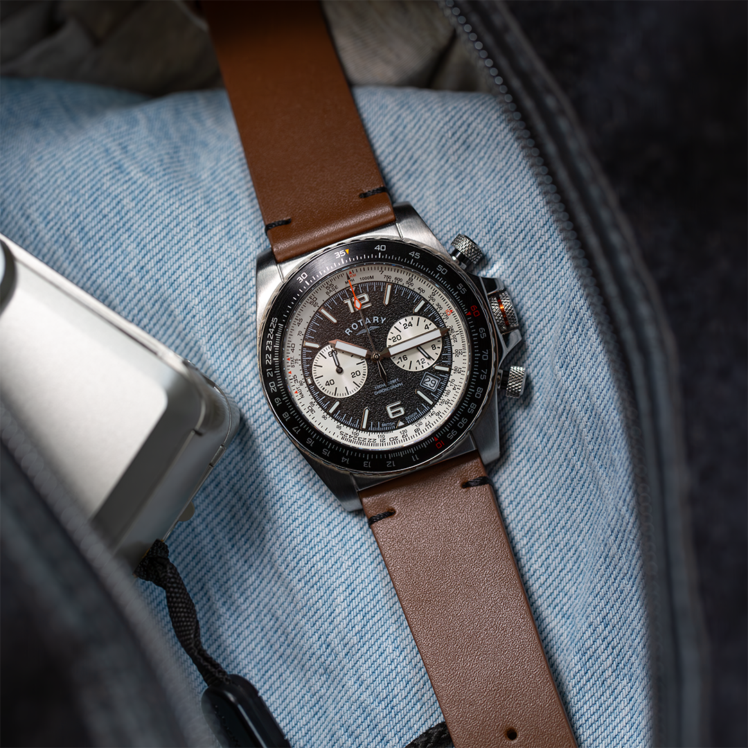 Rotary aeromaster watch in stainless steel with a black dial and bezel. The watch is pictured in a travel bag with a t shirt and a pair of sunglasses