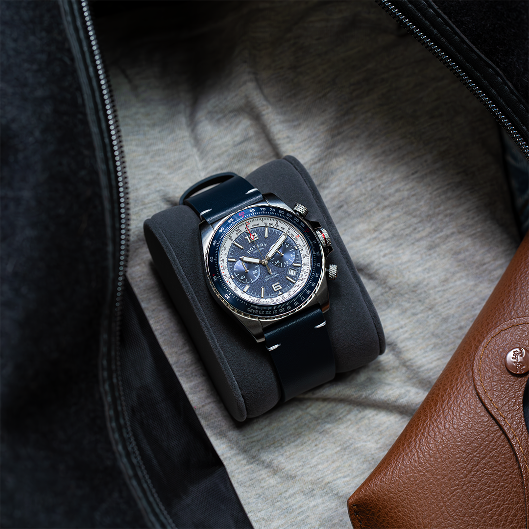 Rotary aeromaster watch in stainless steel with a blue dial and bezel. The watch is pictured in a travel bag with a t shirt and a pair of sunglasses