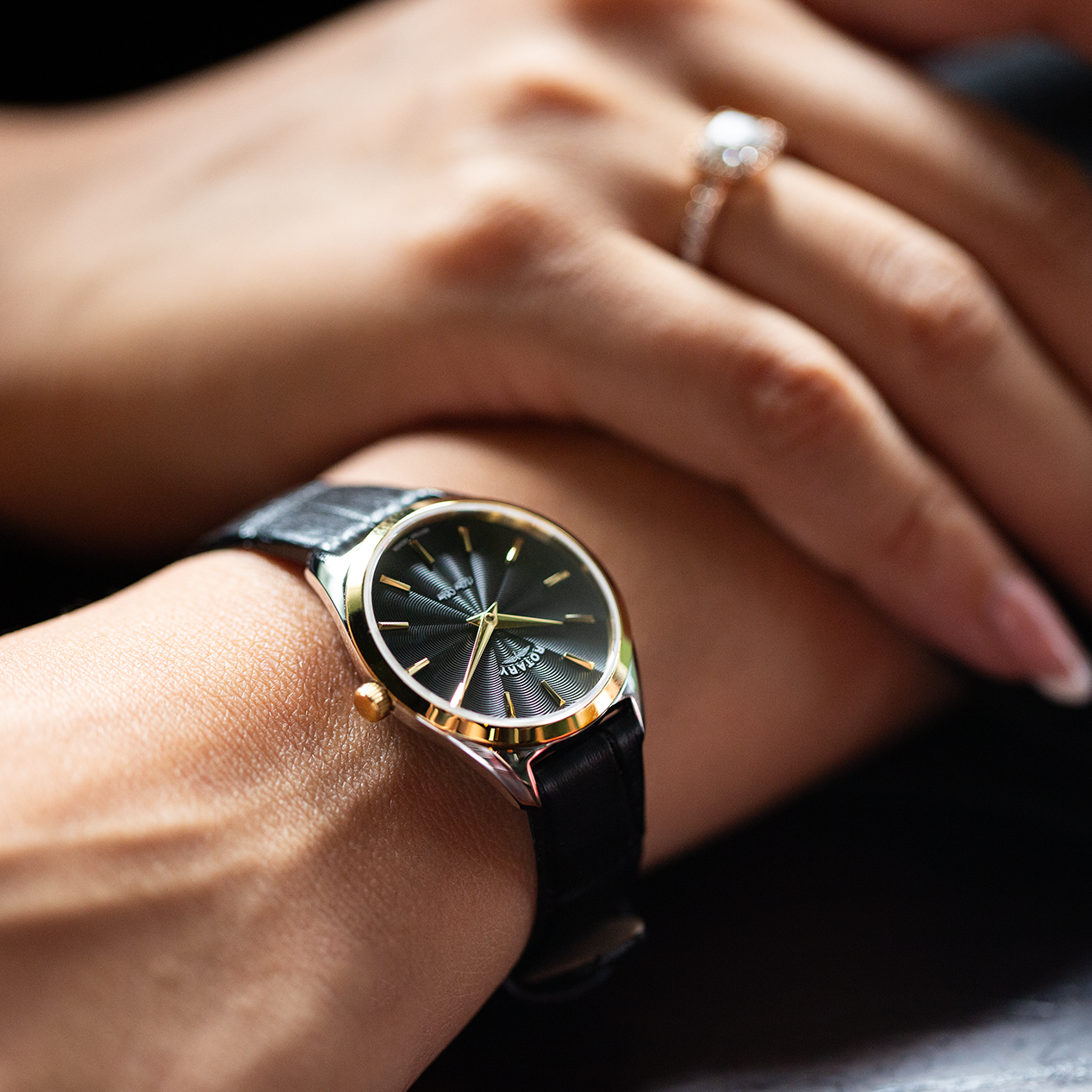 a rotary ladies watch in two tone gold and stainless steel with a black leather strap and black dial being worn by a woman